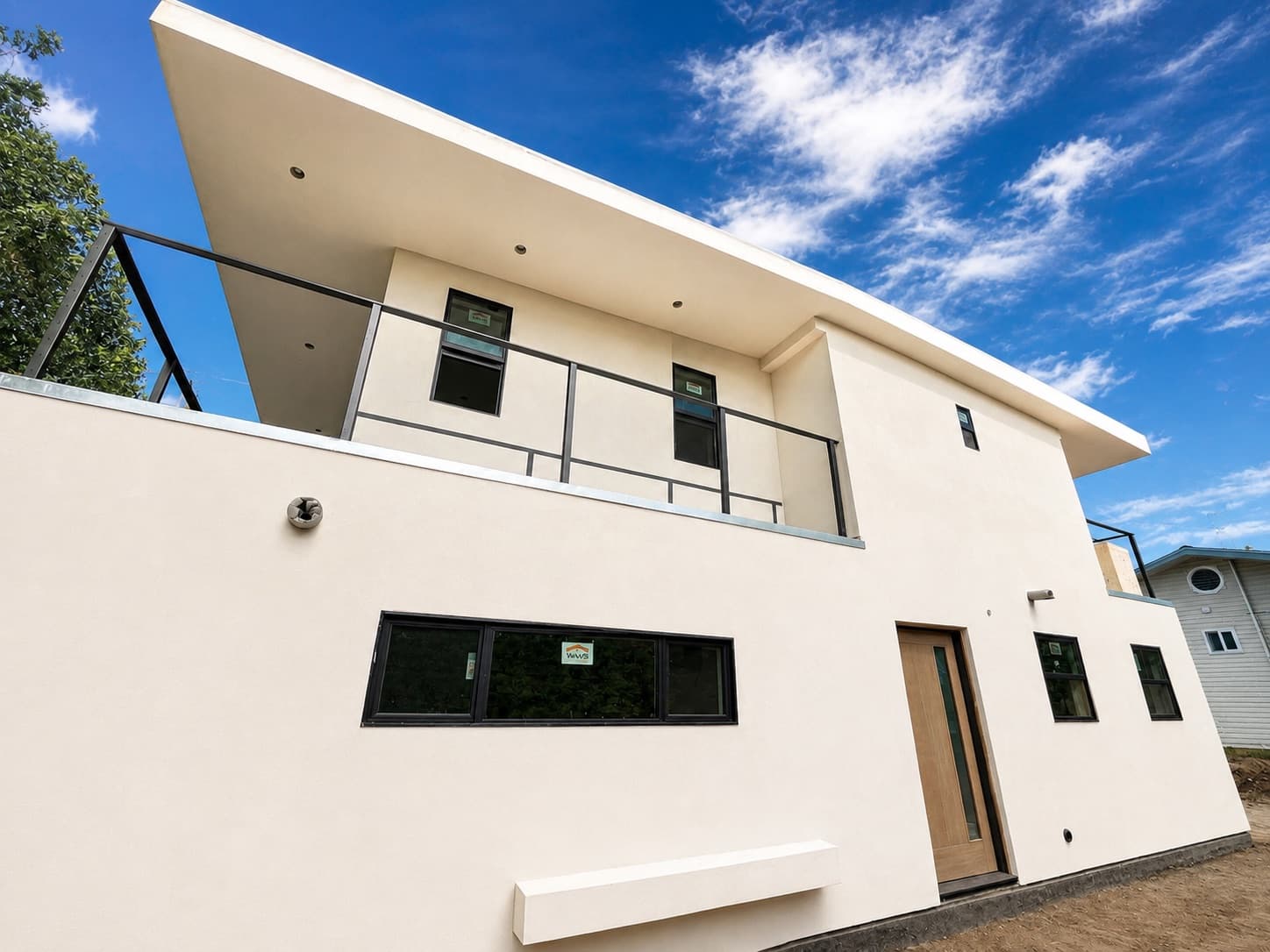 A finished LyteMods two-story steel-framed ADU with cantilevered roof and balcony against a blue sky