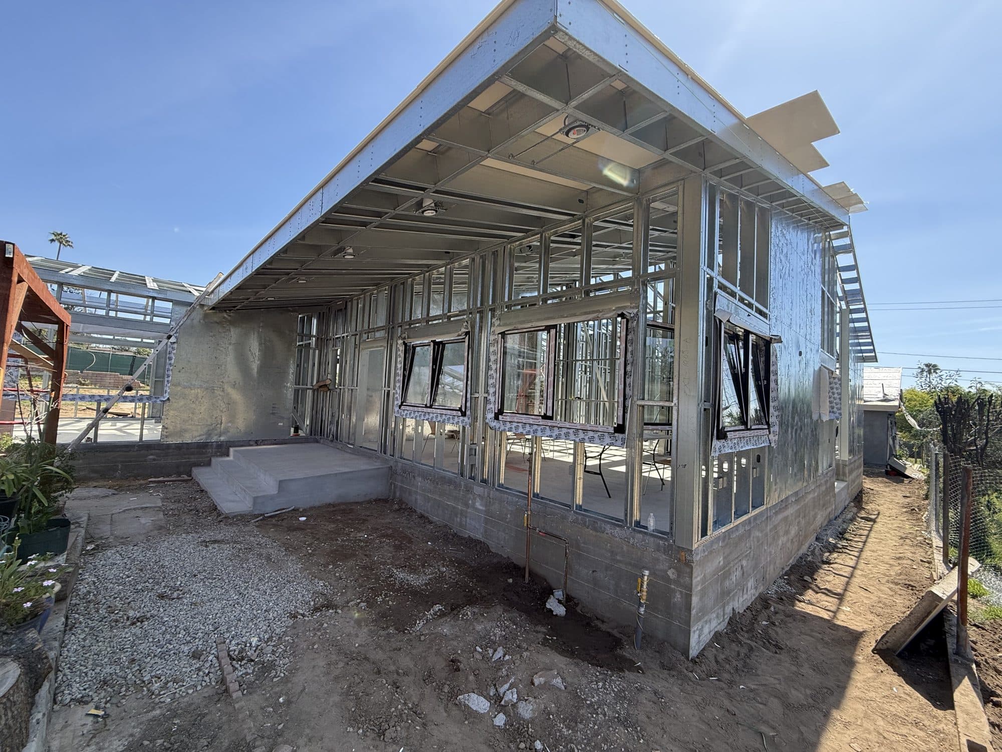 Light-gauge steel frame of the 480 W Palm rebuild, with black-framed windows against a blue sky